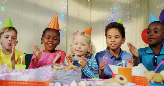 A group of diverse children celebrates a birthday party, with a cake on the table and decorations in the background, with copy space. They are wearing party hats and appear joyful, capturing the essence of childhood celebrations.