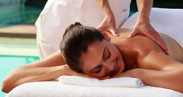 Happy brunette enjoying a massage poolside outside at the spa
