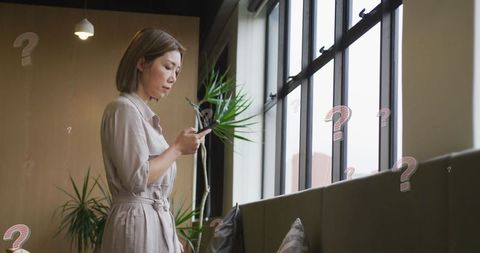 Contemplative Asian Woman Holding Smartphone in Modern Workspace