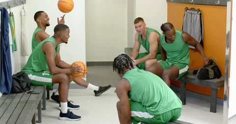 Multiracial basketball team laughing and preparing in locker room before game showing camaraderie