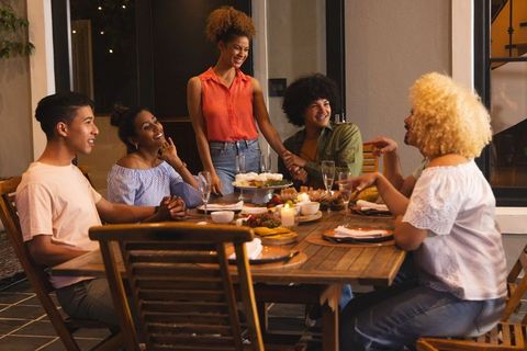 Diverse friends gathering for candlelit outdoor dinner party sharing cake and laughter