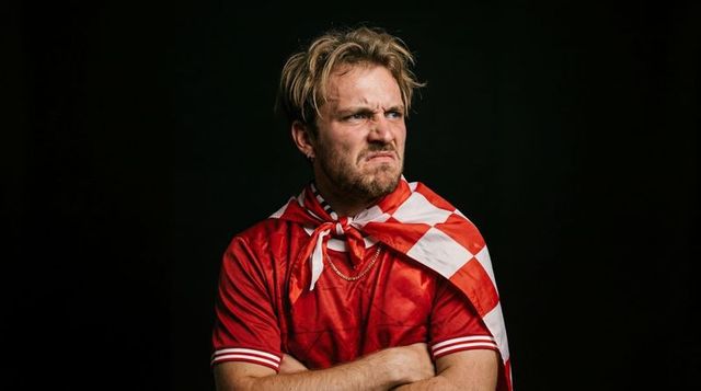 Scowling soccer fan wearing checkered cape and red jersey, intense supporter portrait