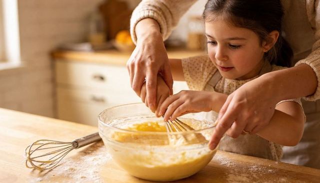 Parent guiding daughter mixing batter in warm home kitchen