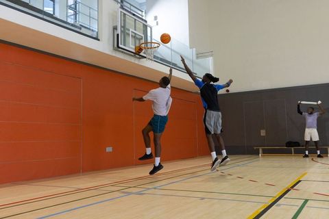 African american teammates jumping for rebound at indoor basketball hoop, dynamic play