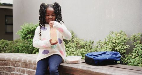 Joyful child opening juice drink outdoors beside backpack