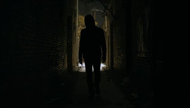 Hooded figure walking through dark urban alley silhouette at night with gritty debris