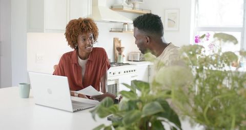 Couple reviewing documents at bright kitchen island, working on laptop and discussing plans