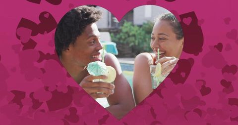 Couple laughing and sipping cocktails at pool rim through heart cutout for romance