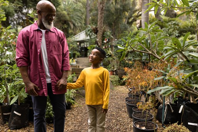 Happy senior african american man with his grandson walking in garden. Spending quality time in garden nursery concept.