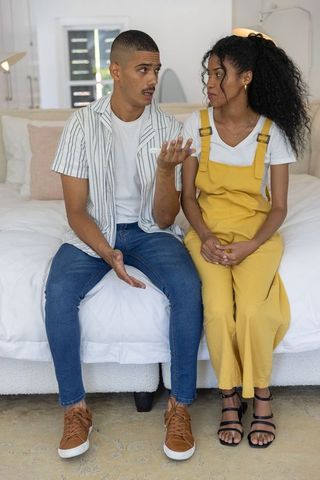 Young couple sitting on bed having serious conversation in cozy modern bedroom interior