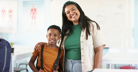 Smiling African American Mentor and Student Standing Together in Bright Classroom