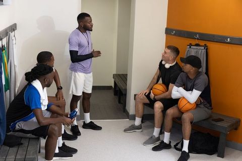Coach leading diverse male basketball team in locker room strategy huddle and motivation