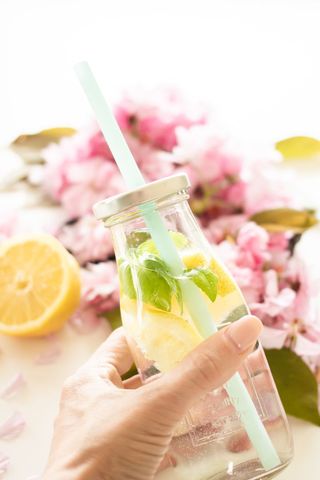 Hand holding fresh lemon basil infused water with blossom background