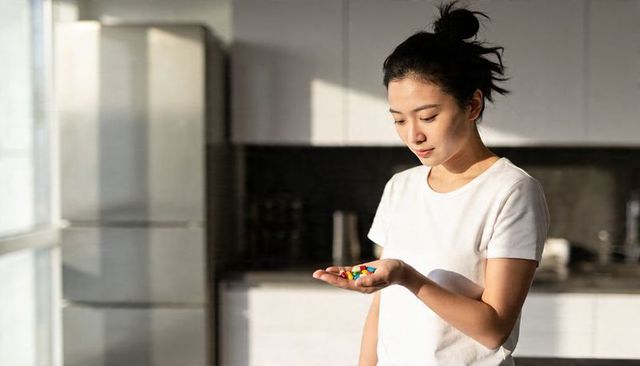 Asian woman holding colorful candy in palm, sunlit minimalist kitchen, quiet morning mood