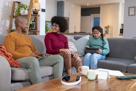 Diverse family sitting on sofa sharing cozy evening while child using tablet