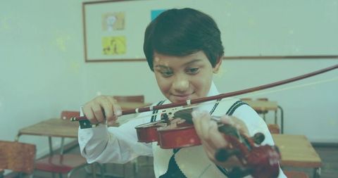 Young boy practicing violin in classroom wearing shirt and vest concentrating on bow technique
