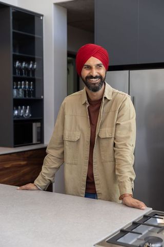 Smiling man in red turban leans on stylish modern kitchen countertop
