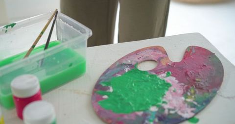 Female artist mixing bright green acrylic paint on colorful palette in home studio