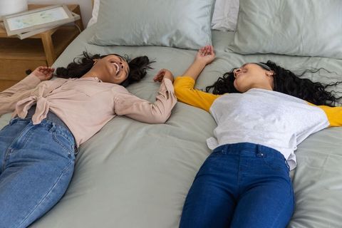Multicultural young women laughing and holding hands while lying on bed