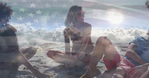 Friends relaxing on sandy beach with american flag overlay, sunset ocean waves, patriotic summer