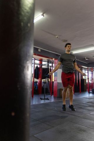 Fit man jumping rope for intense cardio workout in gym with heavy bag and pull-up rig