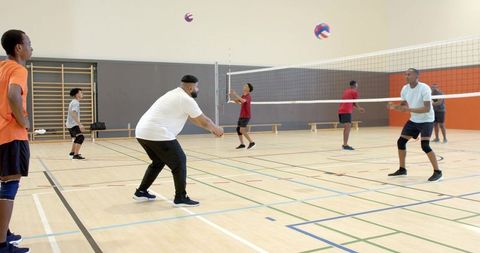 Men playing indoor volleyball passing drill in school gym practicing teamwork