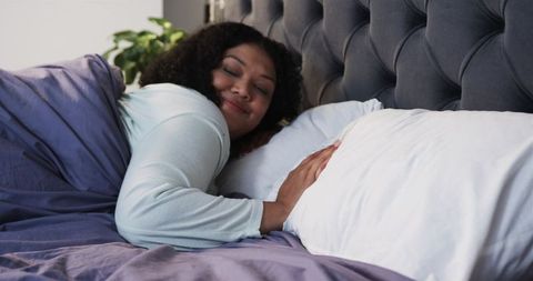 African American woman resting on soft pillow in cozy bed with tufted headboard and plant