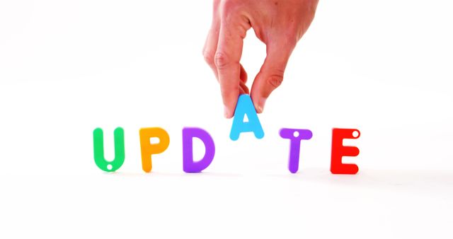 This image shows colorful letters arranged to spell 'UPDATE' with a hand making an adjustment to the letter 'A'. Ideal for concepts of change, improvement, or modification in presentations, articles, or websites. It can also be used in educational materials or apps focusing on learning letters and words.