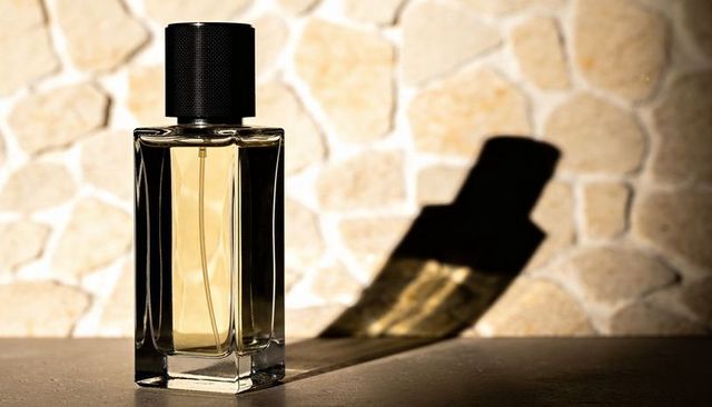 Minimalist rectangular perfume bottle with black cap casting long shadow on sunlit beige tiled wall