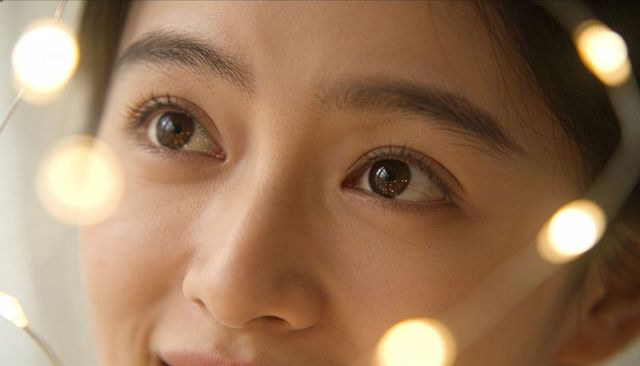 Gazing woman reflecting warm string lights through window glow, intimate closeup portrait