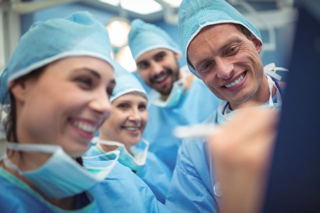 Team of surgeons in surgical attire smiling and discussing in operating room. Useful for illustrating teamwork, healthcare professionals, medical teamwork, and collaborative work environment in medical settings. Suitable for healthcare publications, medical training materials, and hospital promotional content.