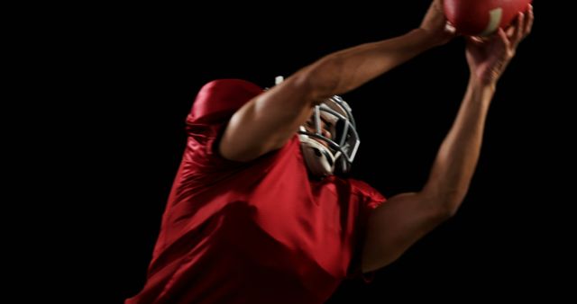 American football player in action wearing red jersey and helmet, catching ball mid-air. Ideal for use in sports-related articles, advertisements, athletic gear promotions, football coaching materials, and dynamic action shots showcasing athleticism and teamwork.