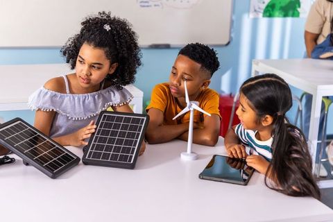 Multicultural elementary students exploring solar panels and wind turbine in stem project