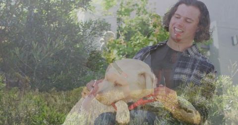 Smiling man petting labrador retriever on lap in sunlit garden, casual outdoor lifestyle