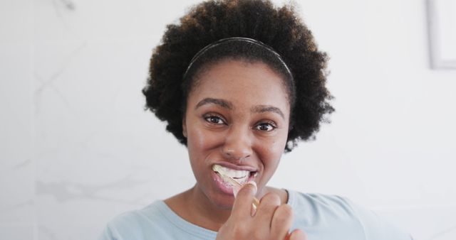 Smiling woman with curly hair brushing teeth in bathroom - Download Free Stock Images Pikwizard.com