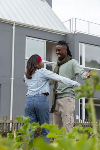 Diverse couple embracing in modern suburban garden by picket fence, joyful reunion