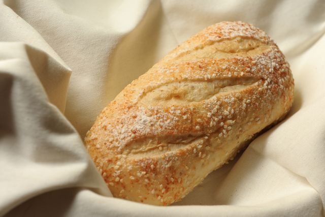 Freshly baked crusty bread resting on white fabric. Perfect for bakery advertisements, food blogs, culinary websites, bakery menus, or artisanal cooking tutorials. Highlights homemade, artisan quality.