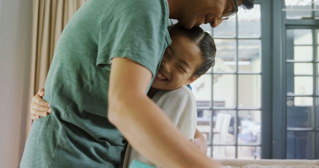 A young Asian girl enjoys a warm embrace with a middle-aged Asian man, her father, expressing joy and affection, with copy space. Their close bond and happy moment together are captured in a cozy indoor setting.