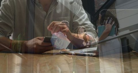Tapping smartphone and collaborating on laptop in glass office with staircase reflections