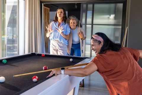 Mature diverse women playing pool in bright modern game room smiling friends billiards