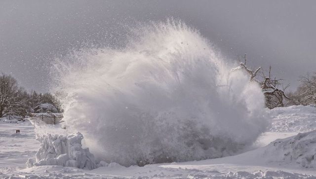Exploding snow plume rising from frozen shoreline in powerful winter gust, dramatic spray