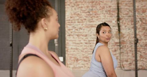 Female friends training together in industrial gym with brick wall and squat rig