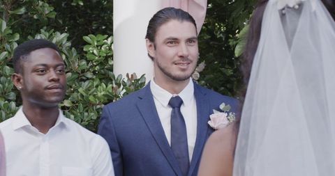 Joyful groom in blue suit smiling during garden wedding ceremony