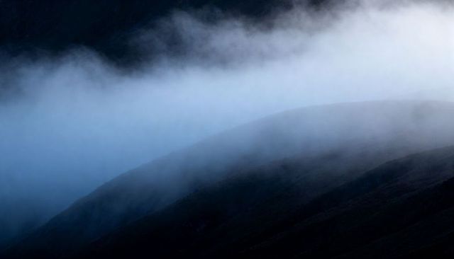 Pale Blue Fog Rolling Over Mountain Ridges, Softening Silhouettes at Dawn