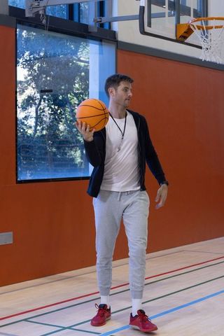 Basketball Coach Posing on Court Holding Ball Near Bright Windows
