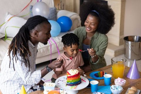 African american family celebrating child birthday with rainbow cake and togetherness