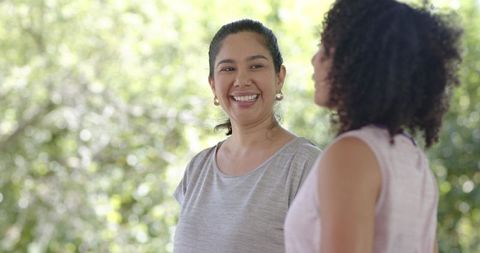 Smiling diverse women chatting in sunny park wearing gold hoop earrings and casual tops