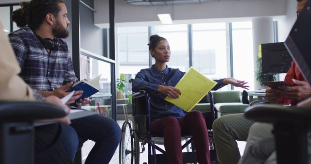 Biracial businesswoman sitting in wheelchair discussing with diverse group of colleagues. working at the office of an independent creative business