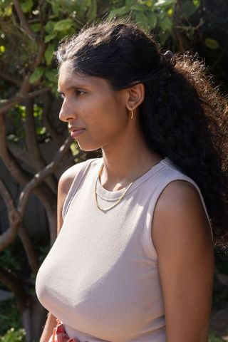 Indian woman standing in sunlit garden wearing ribbed sleeveless top and gold jewelry