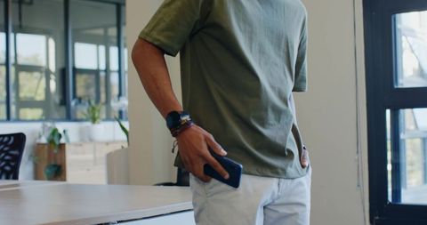 African man standing at modern coworking desk holding smartphone wearing green tee